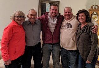 Five family members standing together indoors, arms around each other.