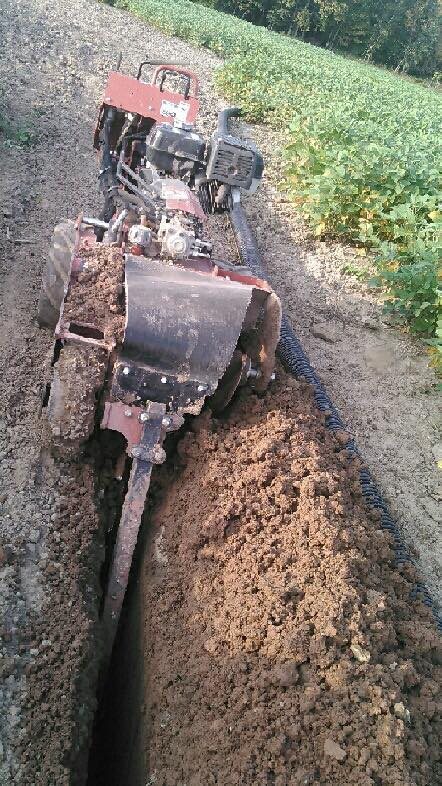 A walk-behind trencher from the rental fleet cutting a narrow trench through garden soil, with fresh earth turned along the run.