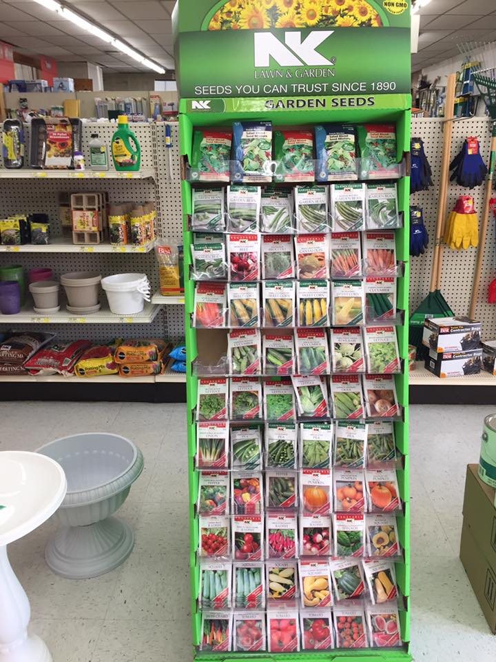 A seed rack and garden supplies in an aisle at Mountain Hardware and Lumber, with pegboard tools, work gloves and planters on the shelves behind.